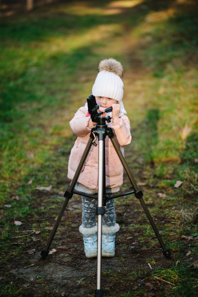儿童调整三脚架拍摄自己的手机或相机的视频。年轻博主的概念。一个快乐的女孩正在为社交媒体搭建三脚架。秋天公园日落时的照片。图片下载