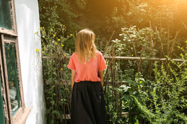 穿着漂亮复古衣服的女人站在老木屋旁边。夏日的乡村风格照片。谷仓或农场附近的院子。图片下载