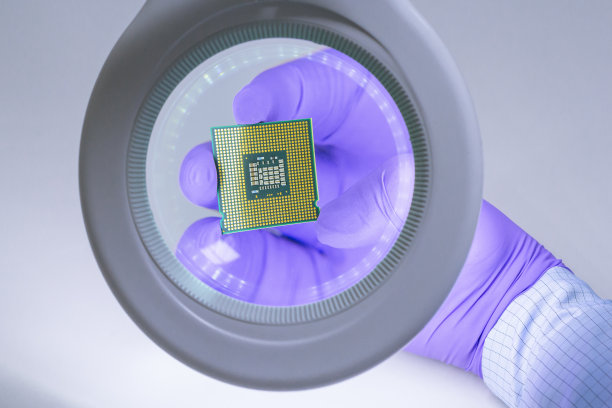 第一人称的观点。一只戴着蓝色手套的手拿着一个处理器芯片，在放大镜下检查它。图片下载