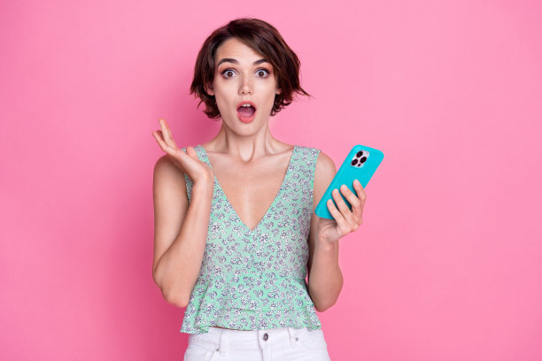 照片中，疯狂震惊的女子拿着智能手机，苹果设备，感谢意外的礼物，粉红色的背景隔离图片下载