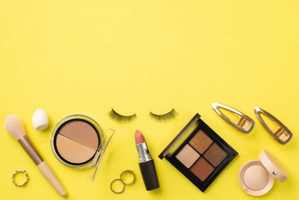 构成的概念。假睫毛黄金发夹戒指化妆刷眼影轮廓调色板小美容搅拌器和口红的照片上孤立的黄色背景与空白图片下载
