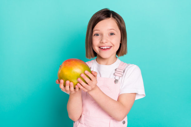 可爱闪亮的女生穿着粉红色整体抱着大新鲜芒果微笑孤立的蓝绿色背景照片图片下载