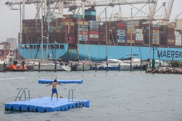 年轻的孩子在科佩尔港前游泳，与集装箱船和一个集装箱码头。卢卡科佩尔是斯洛文尼亚的主要货运港口。图片下载