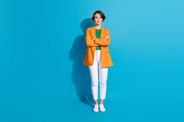 自信的商务女士穿着橙色时尚夹克白裤子的全身照片，在蓝色背景上孤立的图片下载