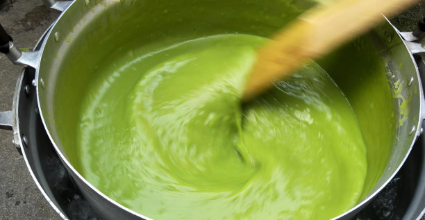 一锅绿色液体用木勺、画笔在一锅水中混合绿色液体的照片。图片下载