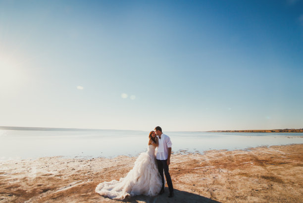 一对新人在海边举行婚礼。阳光明媚的夏日照片。新娘披散着头发，穿着露肩裙。海洋浪漫的仪式。海边的爱情故事。沙子，水和地平线。蜜月拍的。图片下载