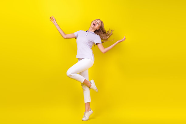 愉快满意的漂亮女人的全身照片，穿着紫色的t恤，踮着脚尖在黄色的背景上跳舞图片下载