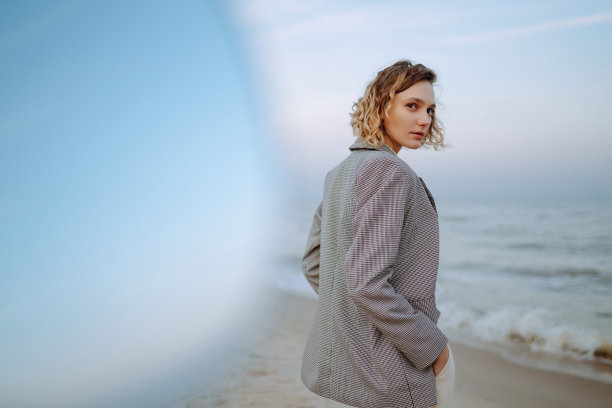 一个秋天的早晨，一位穿着时髦衣服的美女站在沙滩上。图片下载