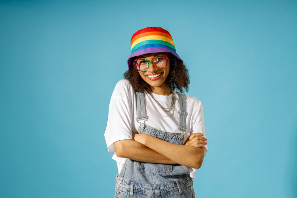 微笑的女人戴着彩虹帽，双手交叉，在蓝色背景下看着镜头图片下载