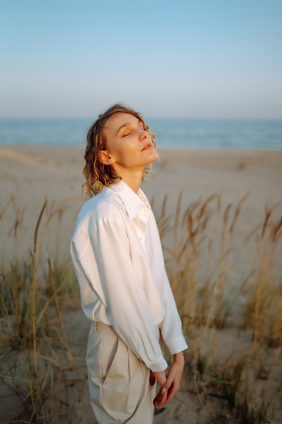 一个秋天的早晨，一位穿着时髦衣服的美女站在沙滩上。图片下载
