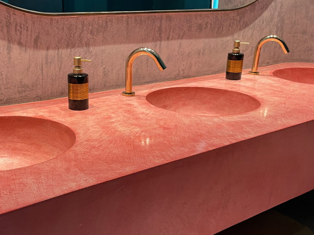 公共卫生间的一排粉色水槽的特写图片，金色的水龙头，镜面墙，洗手液的泵动瓶分配器，卫生，重点放在前景图片下载