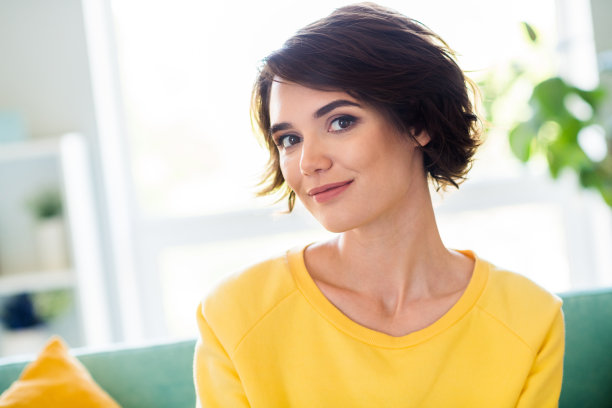 可爱的微笑女孩的照片，穿着黄色时尚的衣服，坐在沙发自己的房间享受舒适的气氛图片下载
