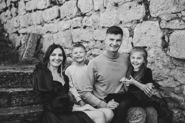 母亲，父亲，女儿，儿子坐在古代宫殿附近的楼梯上。妈妈，爸爸在大自然中拥抱快乐的孩子们。孩子们在老砖墙旁拥抱父母。家人聚在一起。黑白照片图片下载