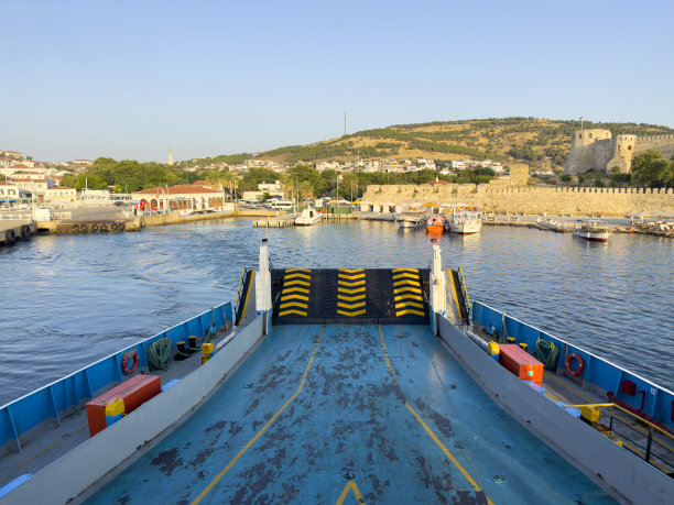 阳光明媚的夏日早晨，空车轮渡驶离博斯加达港。位于爱琴海北部的土耳其岛屿。Bozcaada城堡和城镇的背景视图。图片下载