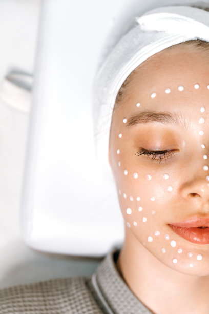 美容的概念。皮肤护理。在一家美容院，一位美丽放松的女性的半张脸的特写垂直照片，她脸上涂着保湿抗衰老霜，以防止过早出现皱纹图片下载