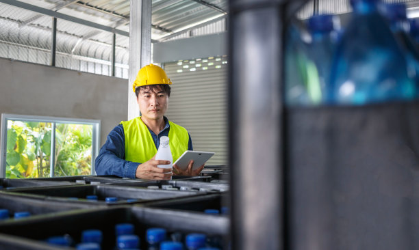 在一家饮水厂，熟练的工程师或质量检查员正在使用平板电脑有效地监控瓶装饮用水的检查过程。图片下载