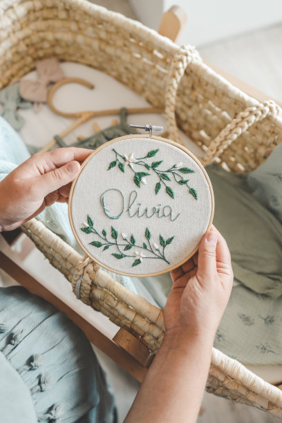 一位孕妇手里拿着手工刺绣，上面写着Olivia的名字，充满期待图片下载