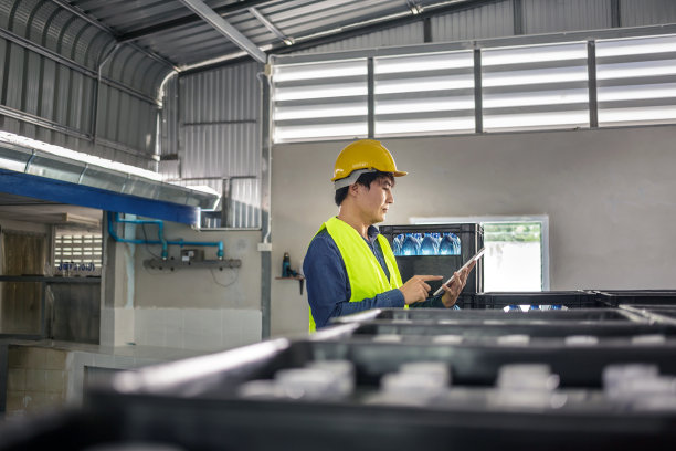 在一家饮水厂，熟练的工程师或质量检查员正在使用平板电脑有效地监控瓶装饮用水的检查过程。图片下载