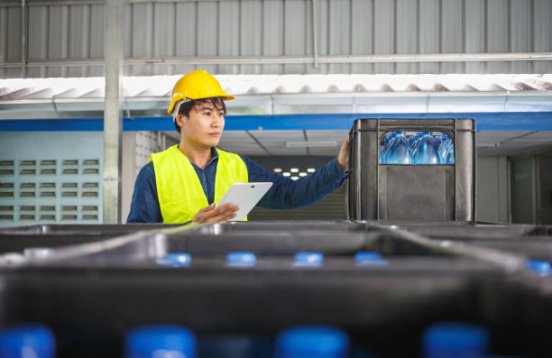 在一家饮水厂，熟练的工程师或质量检查员正在使用平板电脑有效地监控瓶装饮用水的检查过程。图片下载