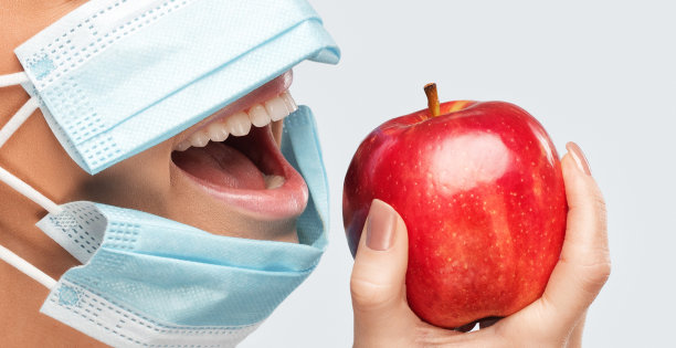 戴面具的年轻女子在办公室吃苹果。卫生保健。图片下载