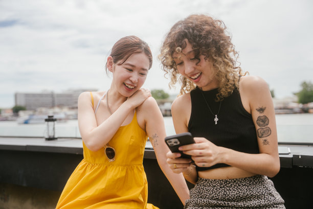 两个亚洲女人在咖啡馆聊天，用智能手机展示照片。两个都笑了起来。图片下载