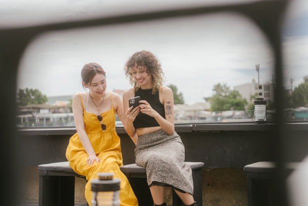 两个亚洲女人在咖啡馆聊天，用智能手机展示照片。两个都笑了起来。图片下载