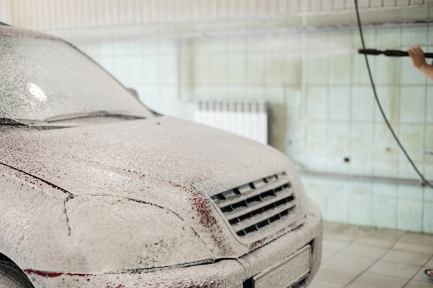 在一个非接触式洗车场，司机用枪喷泡沫。红色的汽车被原子洗衣机的盒子里的肥皂泡覆盖了。那人把车开到洗车店去洗掉车上的污垢和灰尘。图片下载