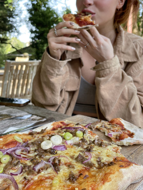 特写照片中，一个面目全非的红发女人在餐厅的露天环境中，吃着一片新鲜出炉的手工脆皮鸭和海鲜酱披萨，木制披萨桨，意大利和中国的融合美食，重点放在前景图片下载