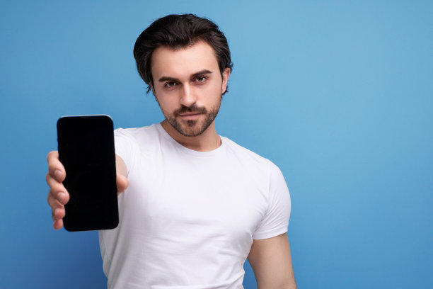 特写照片中，一个留着胡子的黑发男人穿着白色t恤，展示着一个智能手机模型图片下载