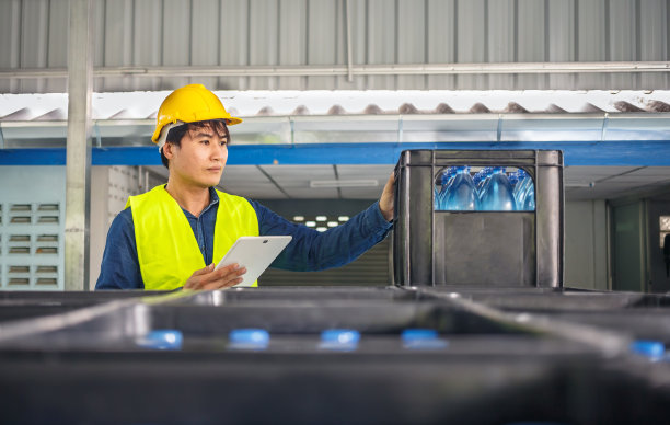 在一家饮水厂，熟练的工程师或质量检查员正在使用平板电脑有效地监控瓶装饮用水的检查过程。图片下载