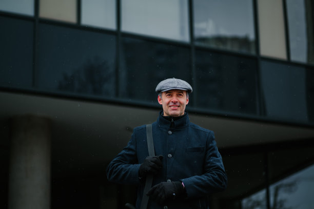 在阴雨寒冷的天气里，商务主管站在商务中心前。图片下载