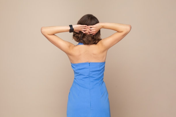 一位留着波浪头发的匿名女子背对着镜头站着，裸露着肩膀，双手一直举着。图片下载