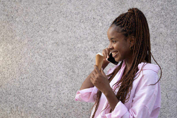 一个快乐的美国黑人女孩一边吃冰淇淋一边打电话。灰色背景隔离图片下载