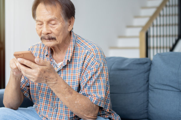 订婚的亚洲老人在家里的沙发上放松时双手拿着手机的肖像照片。图片下载