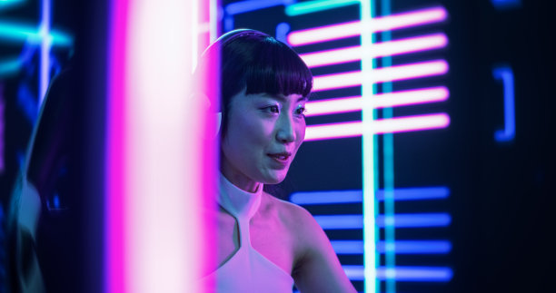 一个时尚的亚洲主播或游戏玩家的肖像，穿着白色的衣服，在未来的霓虹灯房间里与电脑上的互联网订阅聊天。用于社交媒体、流媒体和游戏内容的素材图片下载