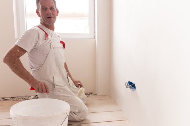 一个人在空房间里用油漆滚筒刷白墙图片下载