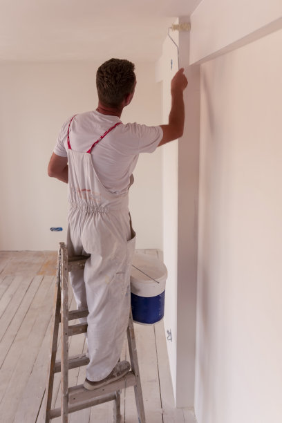 一个人在空房间里用油漆滚筒粉刷白色的墙壁和天花板图片下载