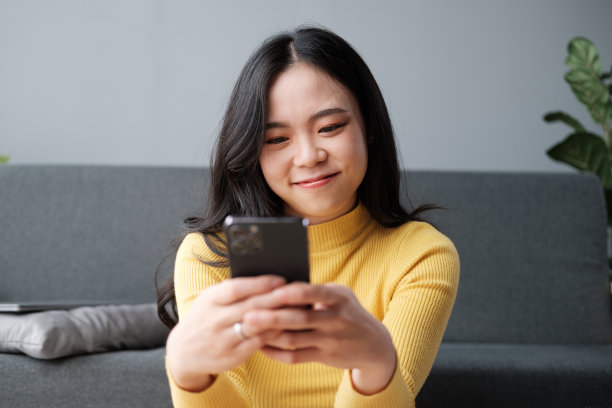 迷人的亚洲女性在舒适的客厅里休息，使用手机，放松，沙发，生活方式图片下载