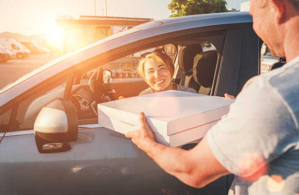 一位年轻的女性坐在汽车的驾驶座上，对着在城市街道上接受两个披萨盒的送货员真诚地微笑。小生意，人际关系，快足餐消费概念照片图片下载