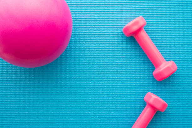 粉红色哑铃和健身球在蓝色瑜伽垫背景健身锻炼的平面。图片下载