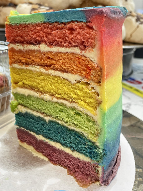 糕饼店陈列甜点的特写图片，彩虹蛋糕片展示了多色的海绵层和黄油冰淇淋，重点放在前景图片下载
