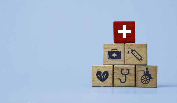 红色方块上的白色十字架在木制堆叠顶部，蓝色背景上的医疗保健图标代表健康和保健概念。图片下载