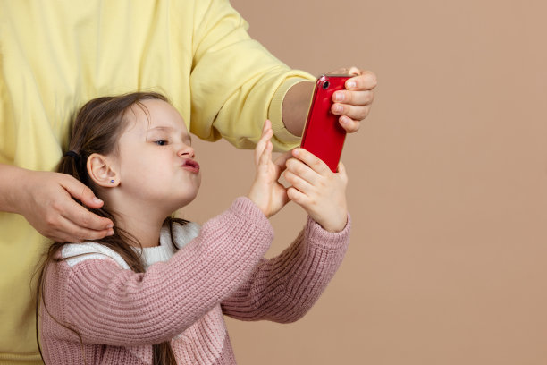 父母从女孩手中拿走智能手机的照片，米色背景。不满的女儿紧握手机反抗。预防儿童电话成瘾的概念，无手机恐惧症图片下载