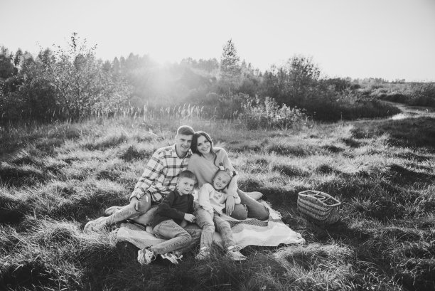 幸福的一家人在大自然中散步，共度时光。妈妈，爸爸，女儿，儿子坐在毯子上，拥抱在田野的草地上，夕阳西下。家庭户外度假。孩子拥抱父母。黑白照片图片下载