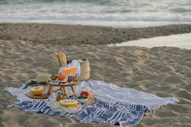 美丽美味的野餐，柠檬水，新鲜水果和牛角面包在日落的海滩。图片下载