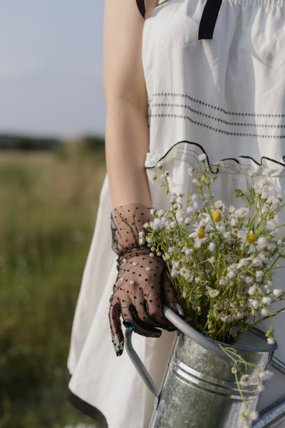 在阳光明媚的日子里，一个无法辨认的女人穿着白色背心裙和雏菊的特写照片。图片下载
