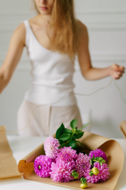 垂直图像的一个年轻女子绑一束粉红色的大丽花包裹在牛皮纸。花艺理念，小而本地经营。图片为您的设计图片下载