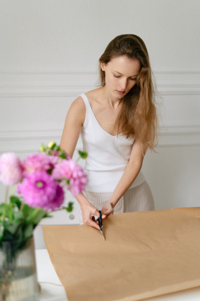 一个年轻迷人的女花店剪牛皮纸与剪刀包裹一束大丽花的垂直镜头。图片为您的设计图片下载