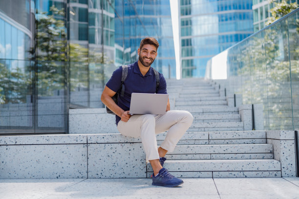 商人坐在楼梯上拿着笔记本电脑，背景是城市摩天大楼。高质量照片图片下载