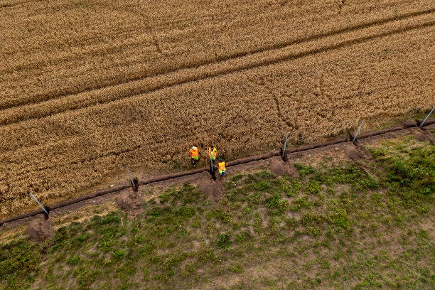 无人机拍摄的建筑工人在高强度高速公路和麦田之间建造围栏的照片图片下载